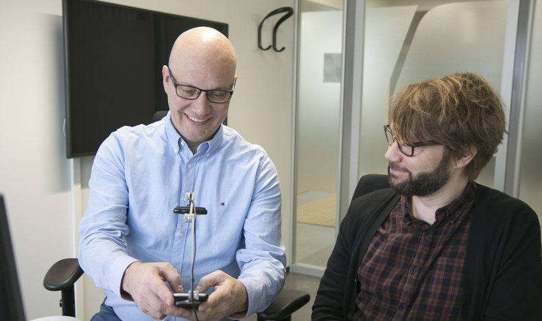 Forskningschef Raino Vastamäki testar en webbtjänst med en mobiltelefon. Ansluten till telefonen finns en kamera som spelar in anvädningen av tjänsten. Bredvid tillgänglighetsexpert Timo Övermark.